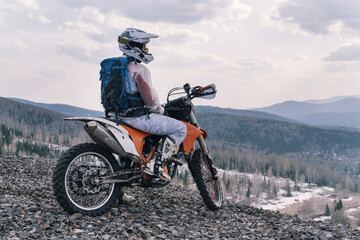 motorcyclist sitting on dirt motorcycle on rubble at the top of off-road mountain relaxing and...
