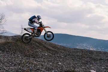 Motorcyclist jumping on dirt motorcycle on rubble mountain top with mountains  view