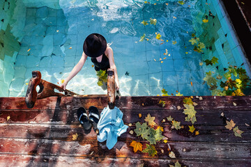 Female wearing  swimsuit and  hat bathing in hot spring pool on sunny day. First frost autumn...