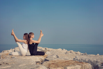 Yoga outdoor. Two beautiful women doing simple yoga asanas on sea shore against the backdrop of a...