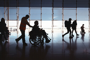 Silhouette Of man Walking With Disabled Person In Wheelchair Airport. People going on flight, large...