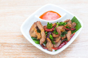 Sun dried pork was served with chili sauce. It's a delicious Thai food on the wooden table.