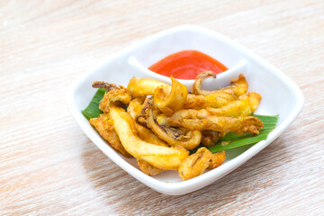 Sun dried squid was served with chili sauce. It's a delicious Thai food on the wooden table.