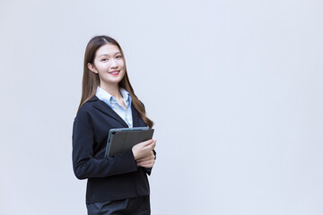 Asian business female in black suit smiles happily while she works and holds tablet on white background.