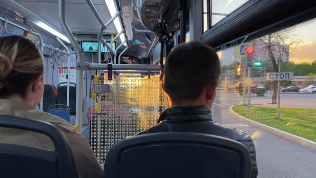 Moscow, Russia - 21 may 2022: Passengers sit inside public transport. Bus stands stops at traffic light. Traveling in bus in Moscow streets at sunset. Spring or summer. Сars driving at the crossroads.