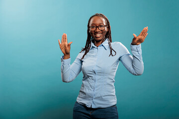 Happy cheerful person being positive while celebrating job promotion with dance. Joyful pleased young woman enjoying dancing and vibing while listening to music playlist on blue background.