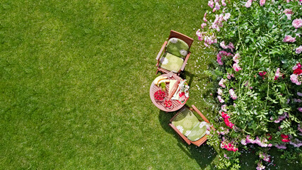 Decorated table with bread, strawberry and fruits in beautiful summer rose garden, aerial drone view of romantic date table food setting for two from above
