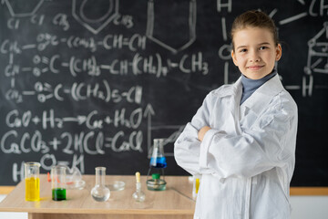 little scientist girl in lab coat with chemical flasks, on school blackboard background with hand drawn science formulas, back to school