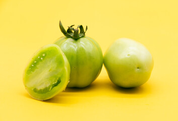 Fresh green unripe tomato isolated on yellow background.