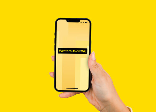Female hand holding a smartphone iPhone with Western Union multinational financial app on the screen. Yellow background. Rio de Janeiro, RJ, Brazil. June 2022