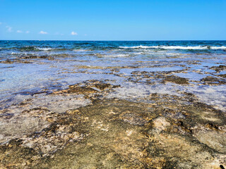 The coast of the Mediterranean Sea, long frozen lava, in the recesses of which there is sea water against a blue sky with clouds.