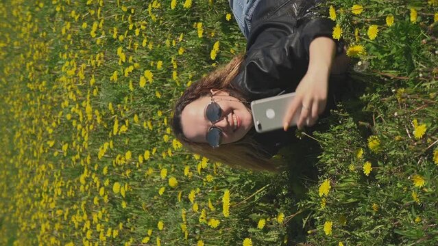 girl takes pictures in the park, lying on the grass. vertical video.