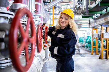Portrait of female refinery worker in safety work wear and yellow hardhat closing valves on gas...