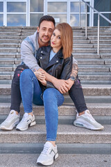 Man hugging his girlfriend while sitting on the stairs outdoors. Relationship and love concept.