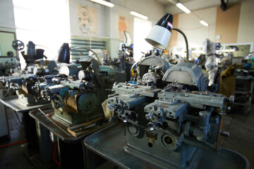Small lathe machines and electric lamps in row used for making small gears of quartz wristwatches, factory shop interior