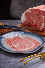 Premium Rare Slices sirloin Wagyu A5 beef with high-marbling texture pick up by bbq tongs with hand from stone plate. Served for Yakiniku, Sukiyaki and Shabu.