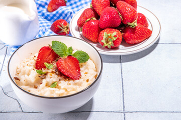 Rice porridge or pudding with fresh strawberry and nuts for breakfast, with plate of strawberries, white tiled background copy space