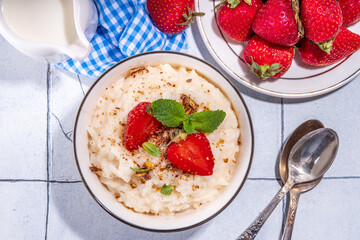 Rice porridge or pudding with fresh strawberry and nuts for breakfast, with plate of strawberries, white tiled background copy space