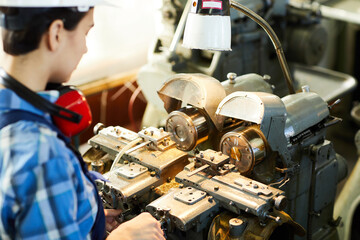 Over shoulder view of busy female engineer adjusting lathe machine for designing details at wristwatch factory
