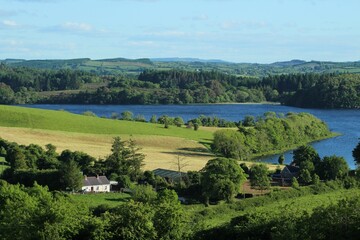 Fototapeta na wymiar Landscape of rural County Leitrim, Ireland at shores of Lough Gill in summertime featuring cottage home nestled amongst fields of farmland pastures bordered by trees