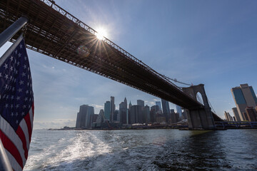 vue sur le pont de Brooklyn à New York avec le drapeau américain au premier plan. Le soleil...