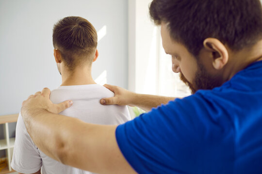 Skilled male therapist examining young man's back and appoints physiotherapeutic treatment. Close up of orthopedist examining man's back in modern health clinic. Health care concept.