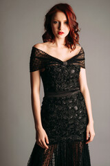 Fototapeta premium Ginger woman in maxi black gown. Candid portrait. Transparent slim shiny dress with v neckline. Stunning look for an event, female fashion. Sexy outfit. Dramatic studio portrait.