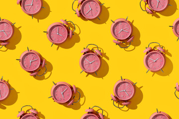 Top view of creative pattern made of pink alarm clocks on a yellow background
