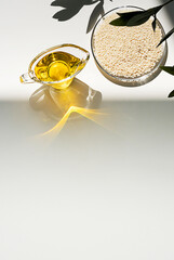 Sesame oil and heap of sesame seeds on white table. Still life of sesame oil and seeds in glass bowl, copy space.