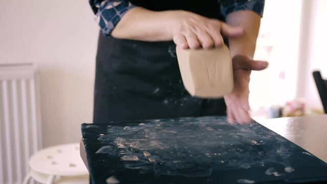 Female hands crumple and roll out piece of clay on table, front view, closeup. Potter prepares clay for processing on table.