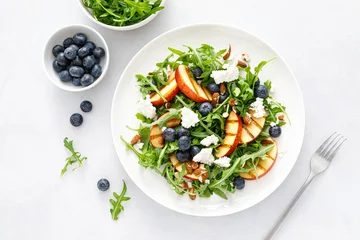 Fotobehang Peach, blueberry and arugula fresh fruit salad with cheese and almond nuts, top view © Sea Wave