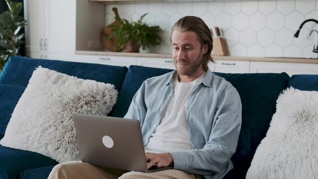 A mam with a laptop looking surprised and exclaiming wow, sitting on a couch.