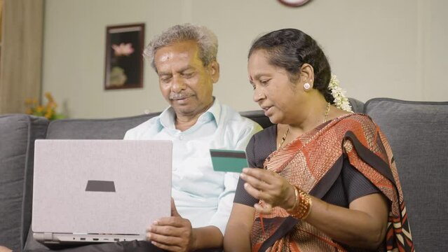 happy senior couple making online payment of e commerce purchase using credit card on laptop at home - concept of shopping, bill payment and banking