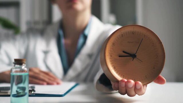 The doctor holds an alarm clock on his hand a hand holds a wooden clock pedantic doctor watches the time of the analog watch arrows. Doctor's office the concept of accurate time doctor shows the clock