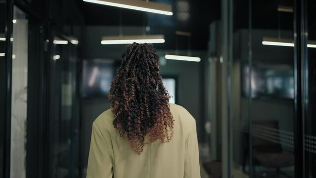 The camera follows the back of a business black woman down the corridor