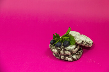 Selected focus. Chocolate cookies with mint leaf and blueberry on pink background. 