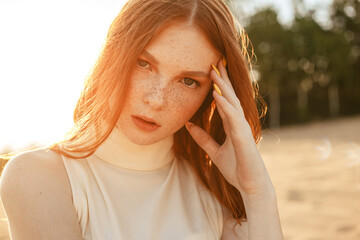 Portrait of stylish female model with ginger hair and natural beauty touching face with freckles...
