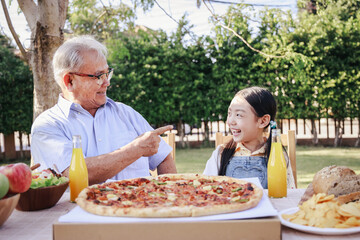 Asian retirement grandfather and pretty granddaughter enjoying to eating pizza together