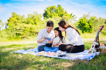Asian parents and little girl looking photo on a smartphone during picnic