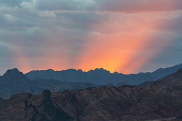 Naklejka na ściany i meble Dramatic scenes with red rays of the sun, cloudy sky and dark silhouette of Sinai mountains. Dahab, Sinai peninsula, Egypt
