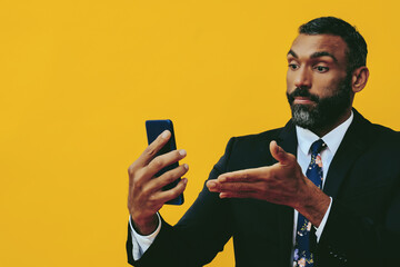 Fototapeta portrait of angry expressive bearded man in suit and tie with smartphone video call pointing hand at camera yellow background studio obraz