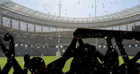 Naklejka premium Colorful confetti falling against silhouette of fans cheering and sports stadium in background