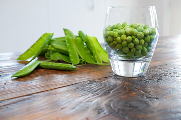 Green peas in glass bowl. fresh pea in the pod with green leaves. green peas on a brown wodden table