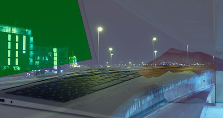 Image of hands of woman using laptop with green screen over sped up traffic in city at night