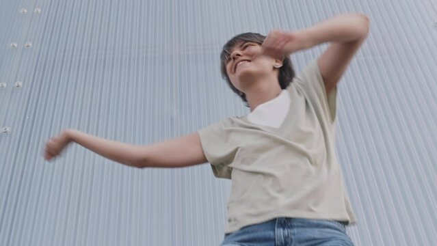 Low angle medium slowmo of short haired young Caucasian woman enjoying dancing on camera outdoors, moving energetically and confidently