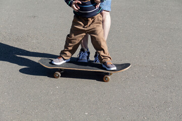 A caring and loving father teaches his three-year-old son to skateboard. A parent spends his free time with his child in the park and on a walk.