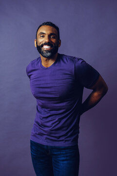 portrait of a handsome smiling man with beard and mustache purple shirt on a gray looking at camera space background studio