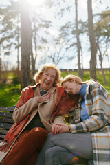 A grandmother is laughing and having fun with her adolescent granddaughter while sitting on the park bench. - 508408267