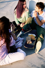 Teenagers sits outdoors, escaping classes and eating fast food at railroad station.