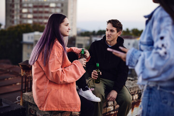 Teenage friends chilling with bottles of beer at roof party.